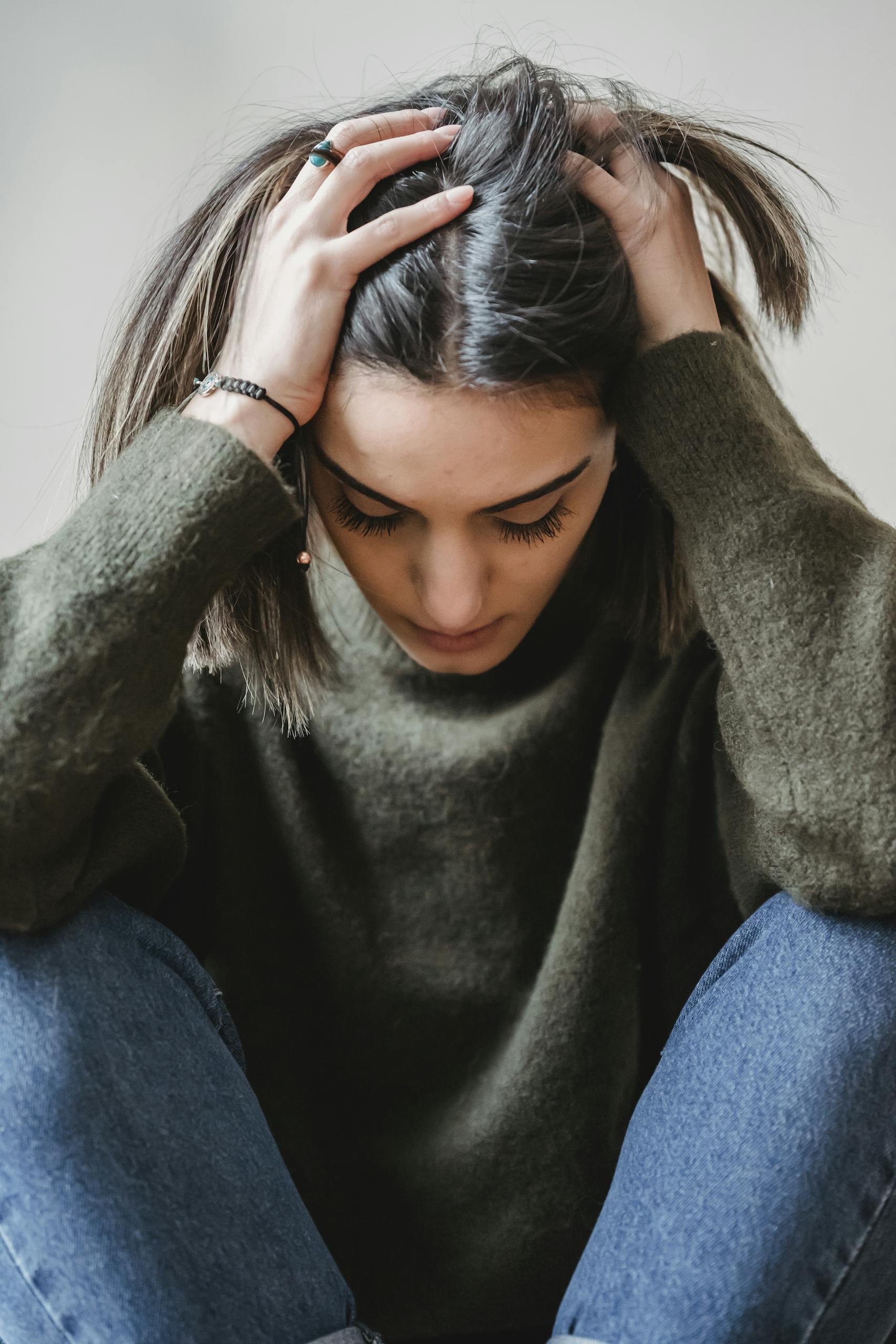 A woman sitting indoors, appearing stressed or upset, touching her head.